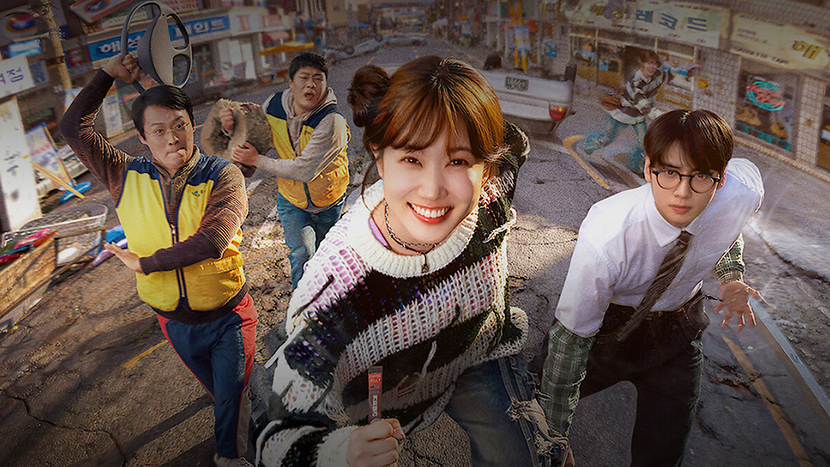 Five people, including a smiling woman in a colorful sweater and a man in glasses, run on a damaged street in a city neighborhood with cracked pavement and rundown storefronts, suggesting urgency or disaster in an urban setting.