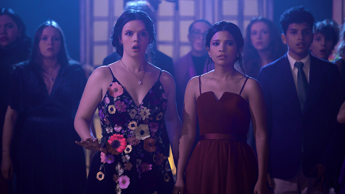 Ellie O’Brien as Grace and Nikki Rodriguez as Jackie wearing dresses in a crowd in 'My Life with the Walter Boys' Season 2.