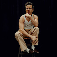 Andrew Scott wears khakis, a white tank, loafers, and a blazer or coat draped over his shoulders.