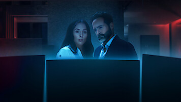 Zuria Vega as Helena and Erik Hayser as Claudio look at a computer screen. 