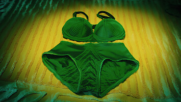 Green women's bra and underwear set laid out on a yellow-striped bedspread under soft lighting.