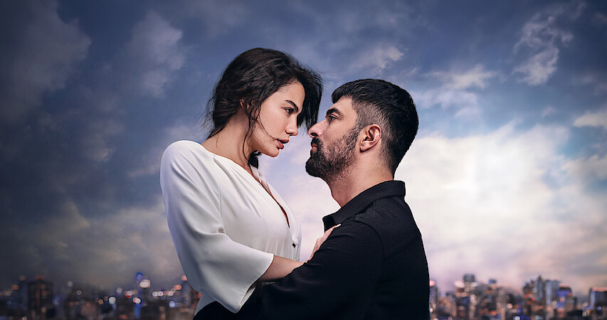 Um homem e uma mulher se abraçam com uma cidade e o céu azul com nuvens ao fundo