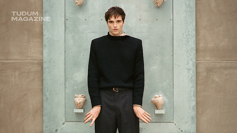 Jacob Elordi stands in front of a blue door while dressed in black.