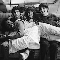 Behind the scenes photo of the cast of ‘Stranger Things 5' sitting on a couch together smiling. 