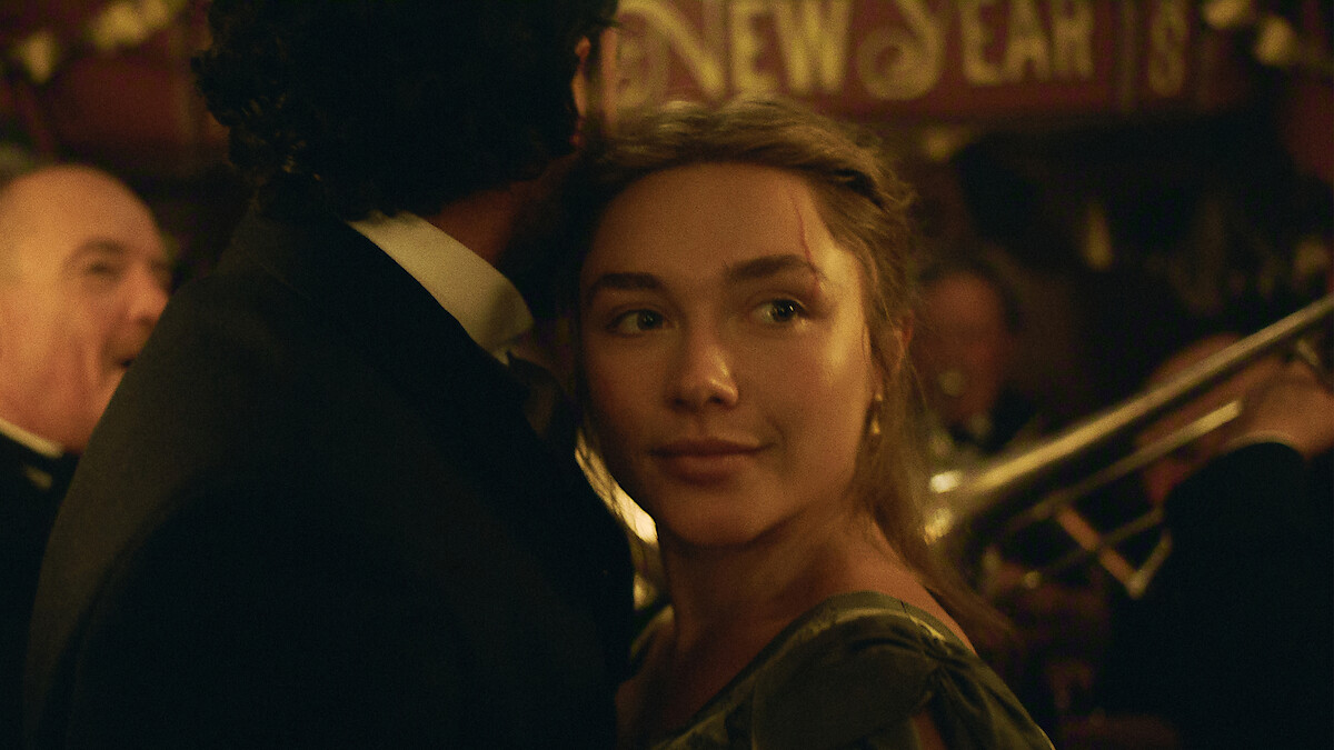A young woman in period clothing dancing with a man at a festive indoor New Year's celebration, with musicians playing brass instruments in the warmly lit background.