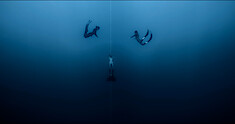Three divers swim in deep waters in a still image from the documentary 'The Deepest Breath.'