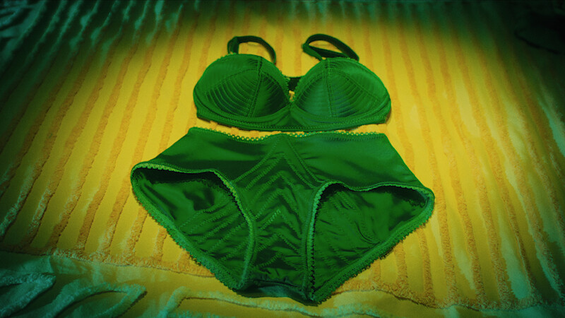 Green women's bra and underwear set laid out on a yellow-striped bedspread under soft lighting.