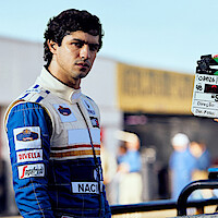 Ayrton Senna (Gabriel Leone) wears a white and blue racing suit behind the scenes of Senna.