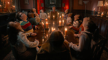 Jamie Campbell Bower as Henry Creel and a group of kids sit around a candlelit table in a dim room in 'Stranger Things 5'