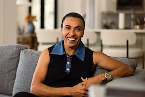 Jogadora de futebol Marta, de cabelos presos para trás, posa para uma foto sentada em um sofá, vestindo camisa preta com gola azul e relógio dourado