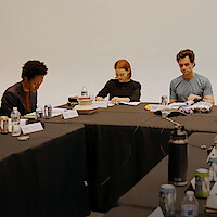 The cast of You Season 5 sitting around a large table with scripts, engaged in a table read.