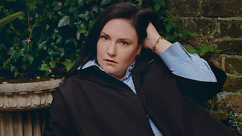 Headshot of Lena Dunham against a brick wall.