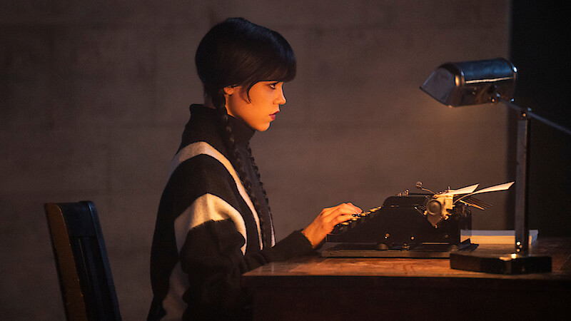 Jenna Ortega as Wednesday Addams sits at a desk with a typewriter.
