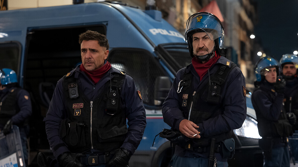 Adriano Giannini as Michele Nobili and Marco Giallini as Mazinga dress in police uniforms and stand outside in front of a police van in the series 'Public Disorder.'