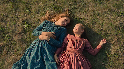 Two girls lay down in a field and laugh.