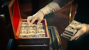 A wooden box filled with cash is handled by someone in white gloves in 'Million Dollar Secret.'