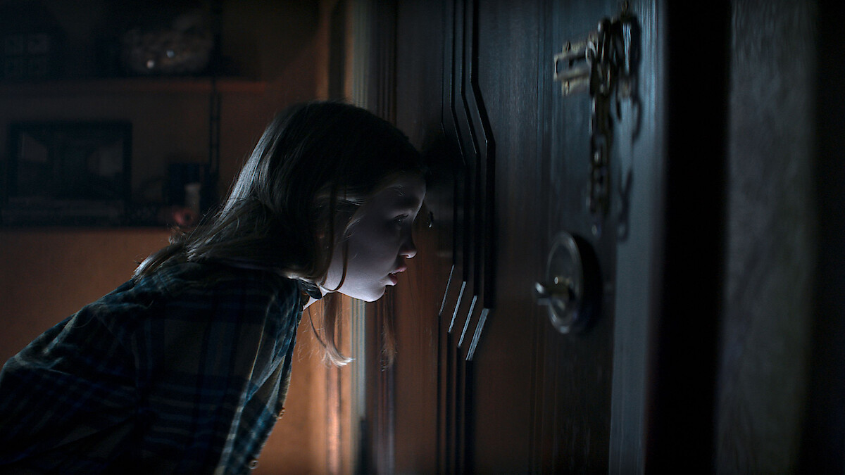 Nell Fisher as Kassie looks through the peephole of a door in an image from the movie ‘Evil Dead Rise.’ 