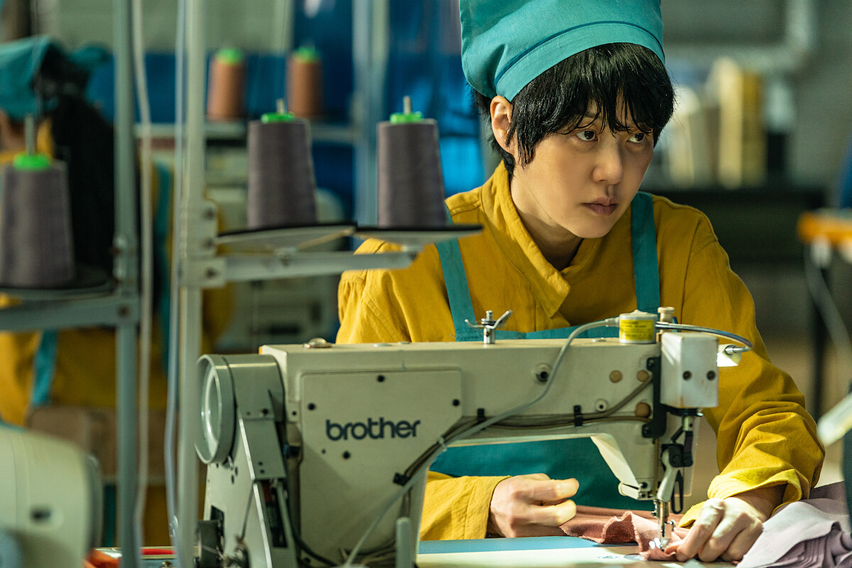 A woman sittin at a sewing machine looking angry