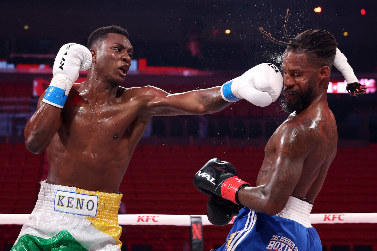 Keno Marley and Diarra Davis Jr. compete in a brightly lit boxing ring, Keno Marley landing a punch on Diarra Davis Jr.'s face. The arena background has red seats and visible branding, with the focus on action and intensity.