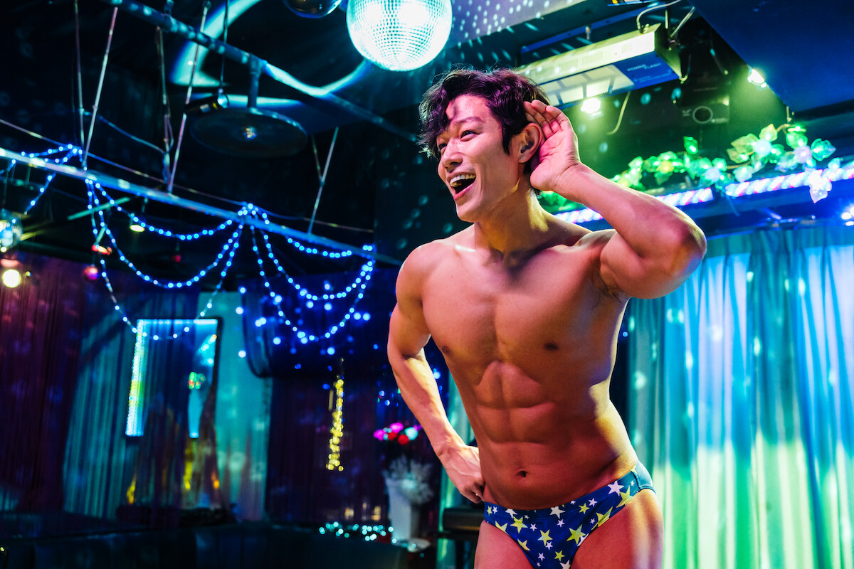 In an image from the film ‘City Hunter,’ actor Ryohei Suzuki as Ryo Saeba wears a star-spangled pair of blue underwear while dancing on a stage lit by neon lights.