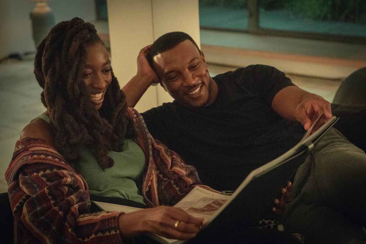 Simbiatu Ajikawo as Shelley and Ashley Walters as Dushane sit on a couch togehter smiling in Season 3 of ‘Top Boy.’