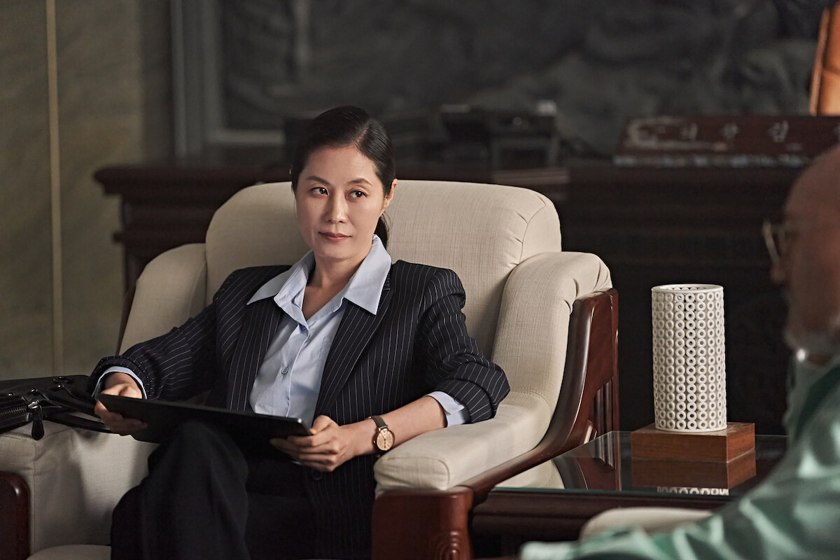 Moon So-ri as Lee Sugyeong wears a pinstripe suit and sits in a cream-colored armchair while holding a tablet in an image from ‘Hellbound’ Season 2.