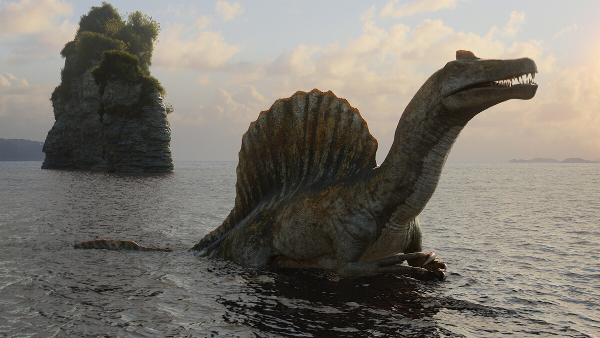 A large spinosaurus dinosaur stands partially submerged in water near a rocky, tree-covered island at sunset, with calm waves and a cloudy sky in the background.