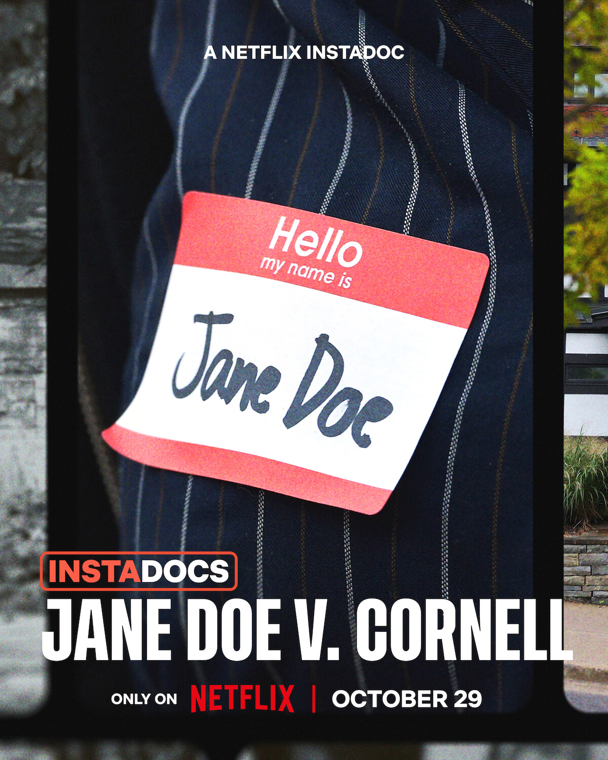 Close-up of a striped suit with a name tag reading "Hello my name is Jane Doe." Promotional image for the Netflix documentary "Jane Doe v. Cornell," releasing October 29. Urban environment background.