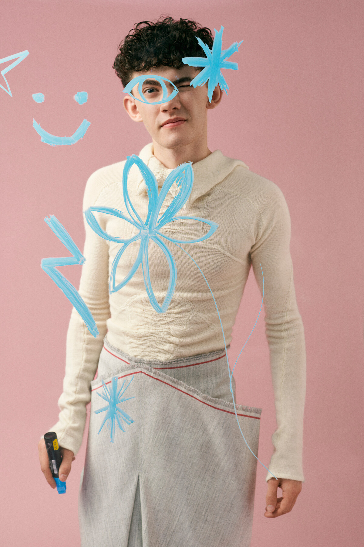Joe Locke from 'Heartstopper' draws blue symbols in front of a pink background.