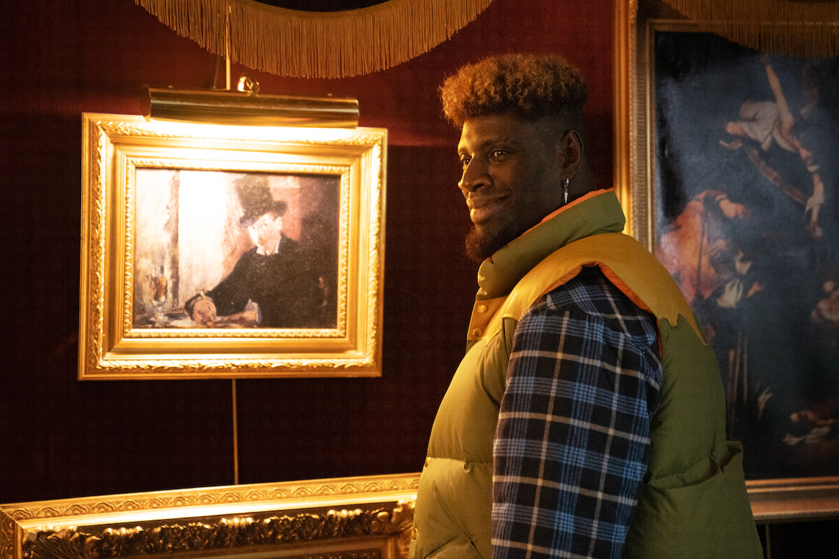 Omar Sy as Assane Diop in disguise stands in front of Manet’s ‘Chez Tortoni’ in Season 3 of ‘Lupin.’
