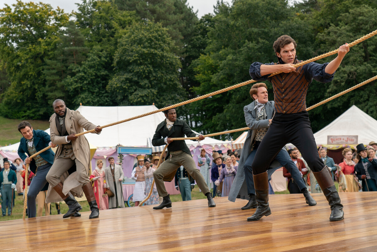 Luke Thompson como Benedict Bridgerton, Martins Imhangbe como Will Mondrich e Luke Newton como Colin Bridgerton seguram as cordas de um grande balão na temporada 3 de ‘Bridgerton’.