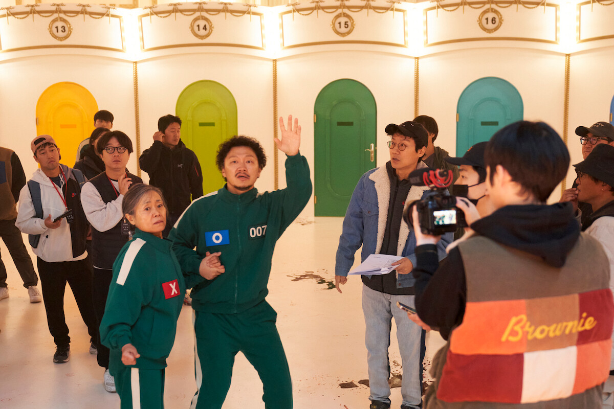 ‘Squid Game’ Season 2 set with players in green tracksuits against colorful doors.
