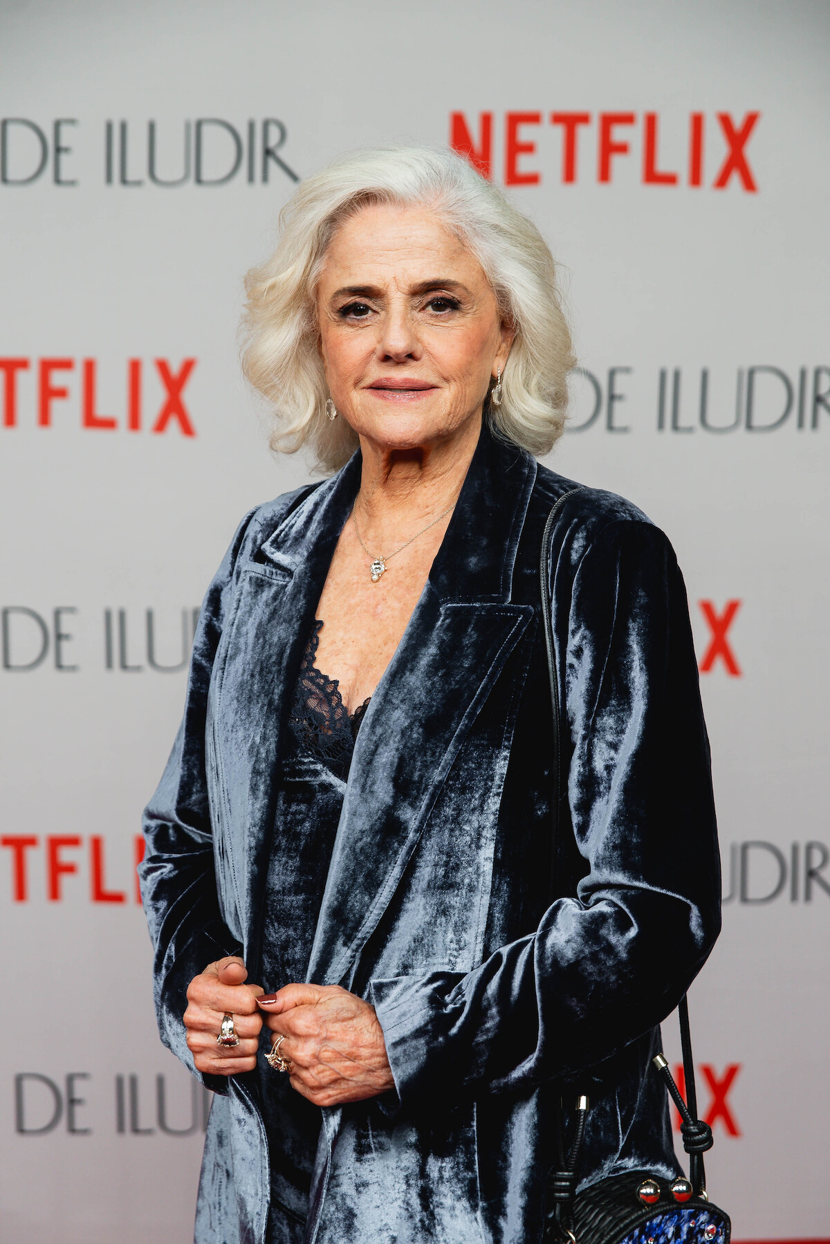 A atriz Marieta Severo é uma mulher branca e de cabelos grisalhos. Ela veste um conjunto de calça e sobretudo azul e preto