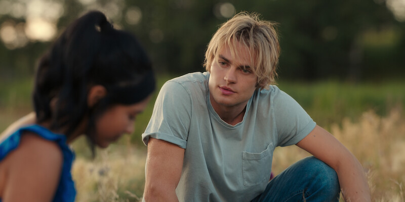 Nikki Rodriguez as Jackie and Noah LaLonde as Cole sit in a field together in Season 1 of ‘My Life with the Walter Boys.’