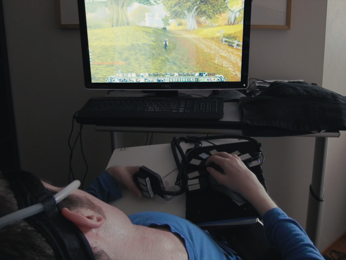 Mats Steen wears a blue shirt and plays a video game in a dark room.