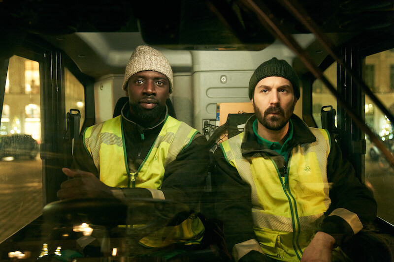 Omar Sy as Assane Diop and Antoine Gouy as Benjamin Ferel wear yellow vests and drive a truck in Season 3 of 'Lupin.'