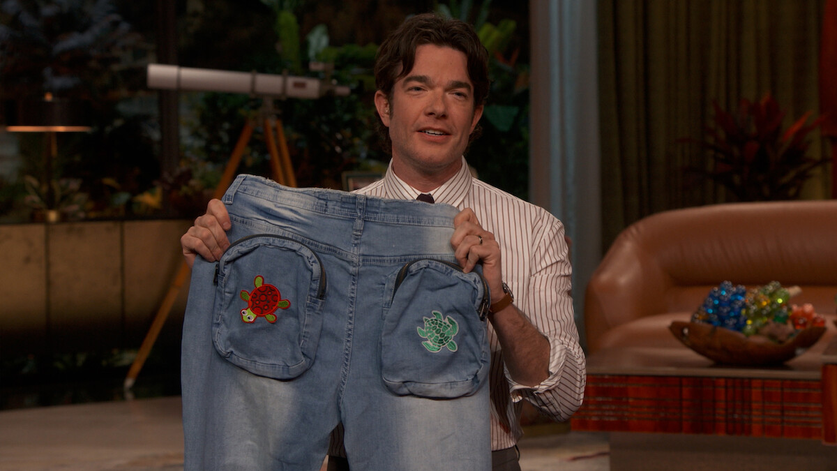 John Mulaney holds up a pair of jeans.