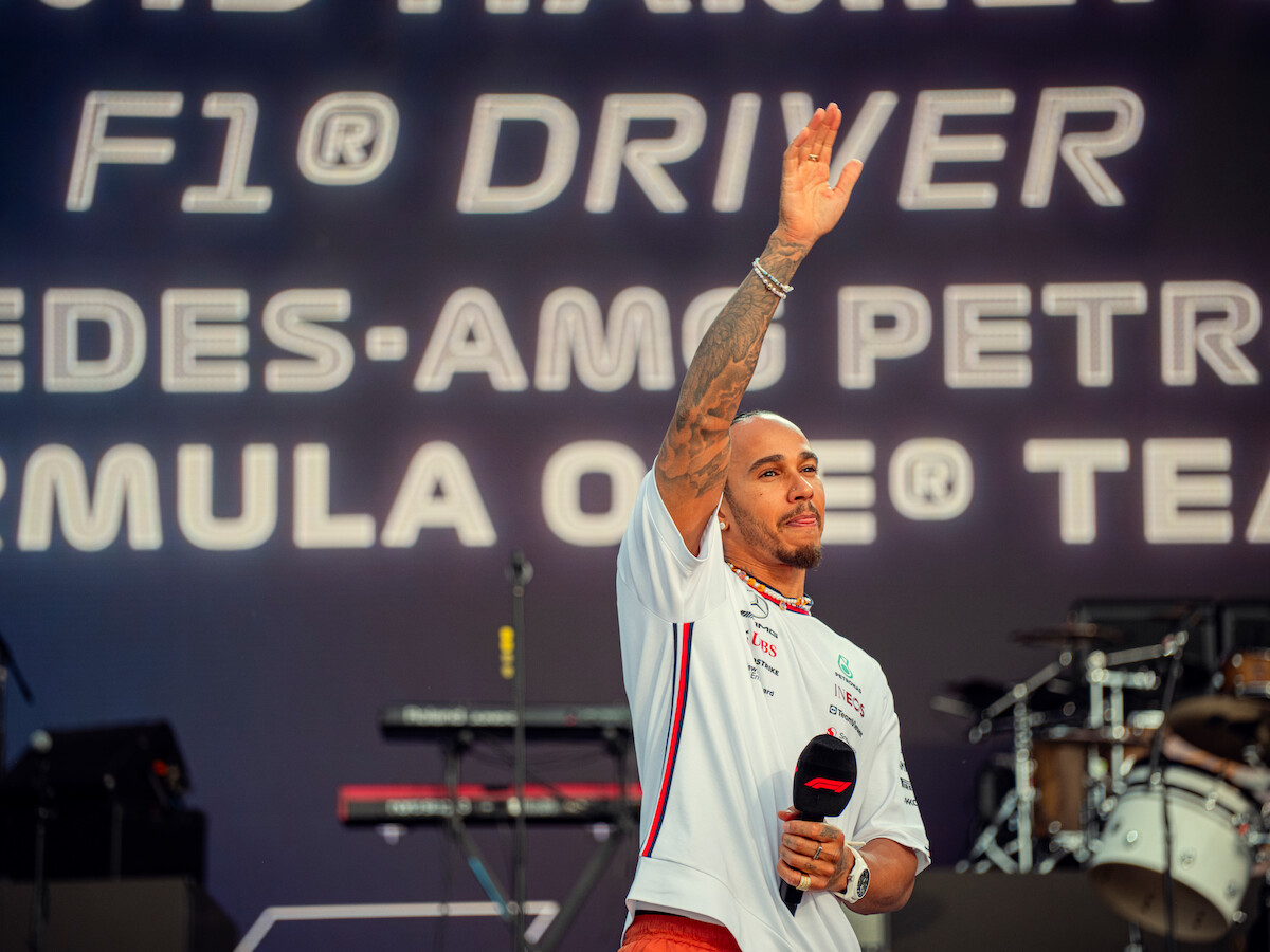 Lewis Hamilton waving while holding a microphone in his hand.