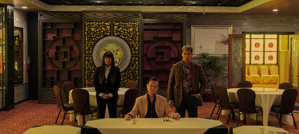 Johnny Kou as Big Sun sits at a table for a meeting in an ornate restaurant shrouded in golden light in season 1 of ‘The Brothers Sun’
