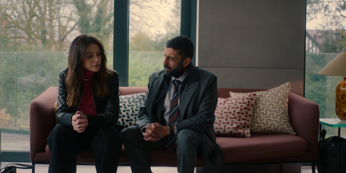 Michelle Keegan as Maya Stern and Adeel Akhtar as Sami Kierce sit on a couch in the series ‘Fool Me Once.’
