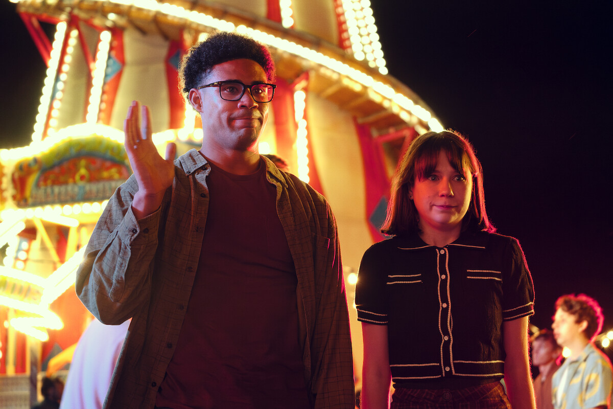 Darragh Hand as Michael and Jenny Walser as Tori stand together at a carnival with awkward expressions in Season 3 of ‘Heartstopper.’