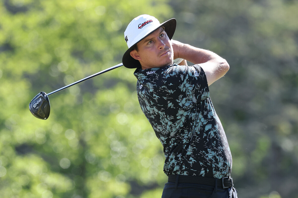 Golfer Joel Dahmen keeps his eyes on the ball after a drive, while wearing a bucket hat inscribed with the word “Cancer” crossed out.