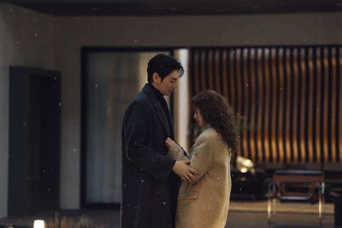 Um casal sul-coreano se abraça em uma sala com iluminação baixa