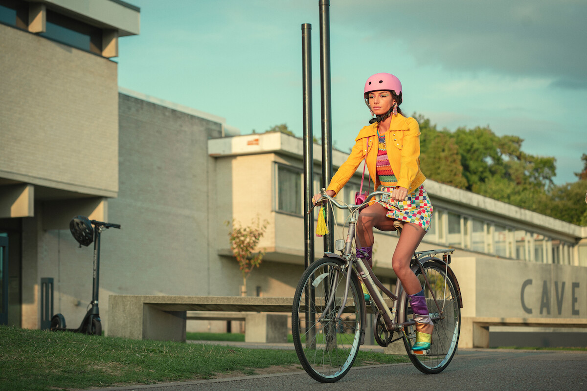 Mimi Keene as Ruby rides her bike to school and wears a colorful outfit in Season 4 of ‘Sex Education.’