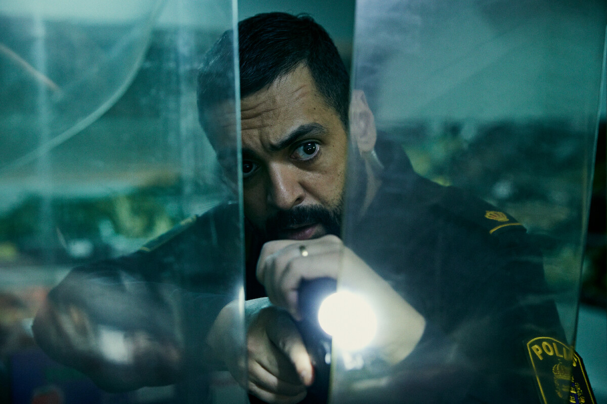Ardalan Esmaili as Farid holds up a gun and flashlight in ‘Deliver Me.’