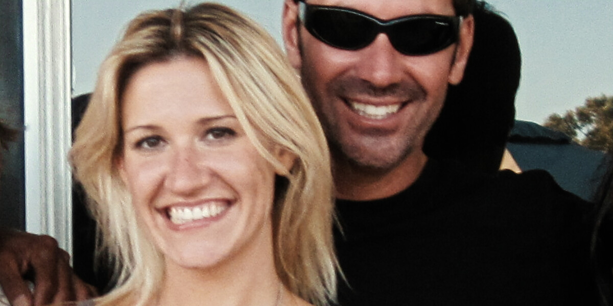 Smiling woman with blonde hair and a man in sunglasses standing close together outdoors, both appearing happy with sunlight and greenery in the background.