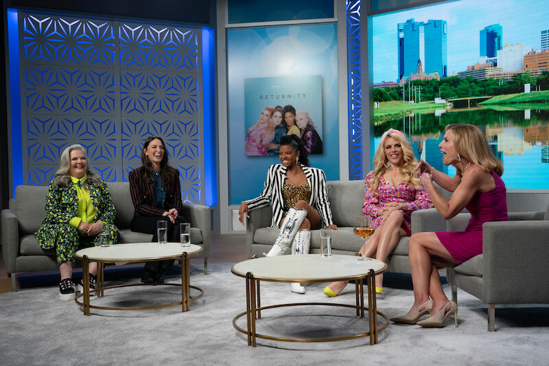 Paula Pell as Gloria, Sara Bareilles as Dawn, Renée Elise Goldsberry as Wickie, and Busy Philipps as Summer sit together on the stage of a talk show in Season 3 of 'Girls5eva'