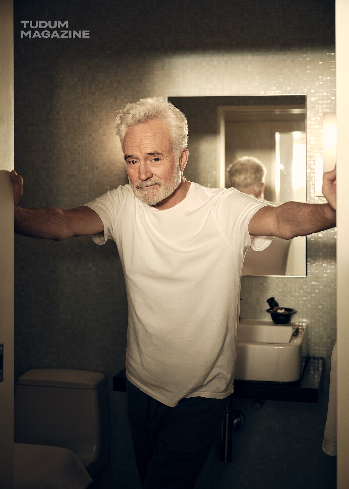 Bradley Whitford se apoiando na entrada de um banheiro
