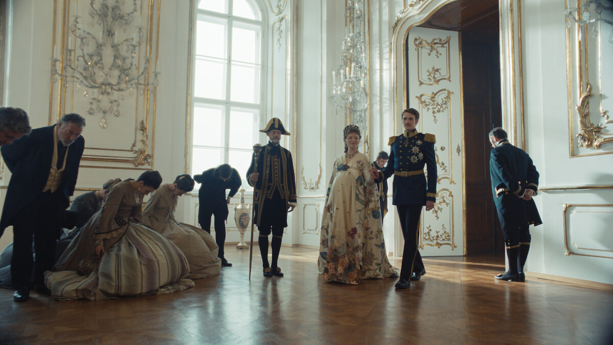 Devrim Lingnau as Empress Elisabeth of Austria and Philip Froissant as Emperor Franz Josef walk in a grand room together while courtiers bow to them in Season 2 of ‘The Empress.’