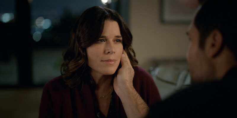A woman looks thoughtfully at a man who gently holds her face, sitting together in a softly lit, cozy indoor setting at night, conveying a sense of intimacy and emotional connection.
